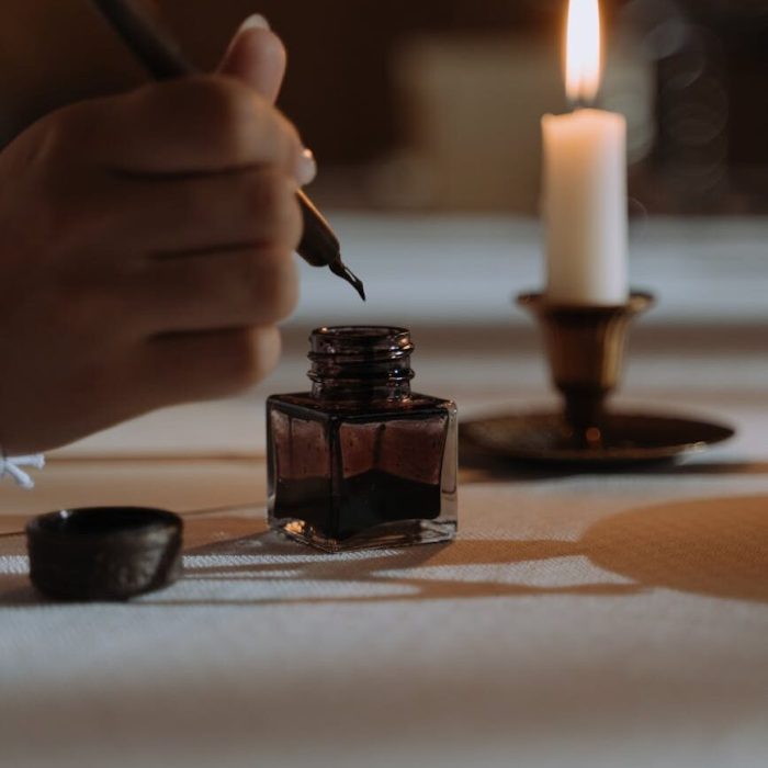 person dipping quill pen in an ink